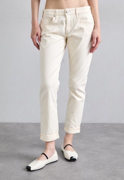 Pantaloni in denim color crema con taglio slim e polsini arrotolati, abbinati a scarpe basse bianche e nere con una fascia sul dorso del piede.