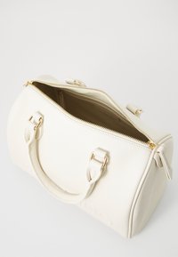 White textured leather duffle bag with gold hardware, double handles, and a zippered opening, featuring a spacious interior.