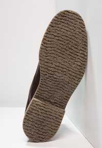 Suela de zapato marrón oscuro con agarre de goma texturizada, que presenta un patrón en forma de ola y un ligero desgaste, con la talla visible cerca del talón.