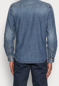 Denim-paita keskisinisenä, pitkät hihat, napilliset kalvosimet, terävä kaulus ja kaartuva helma. Ominaisuuksiin kuuluu haalistunut tekstuuri ja vahvistetut ompeleet.