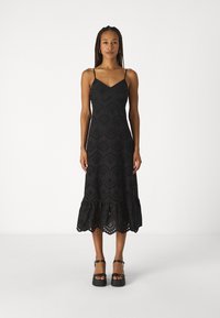 Vestido preto sem mangas com decote em V, apresentando padrões de bordado à vista, uma barra godê e uma borda rendada na parte inferior.