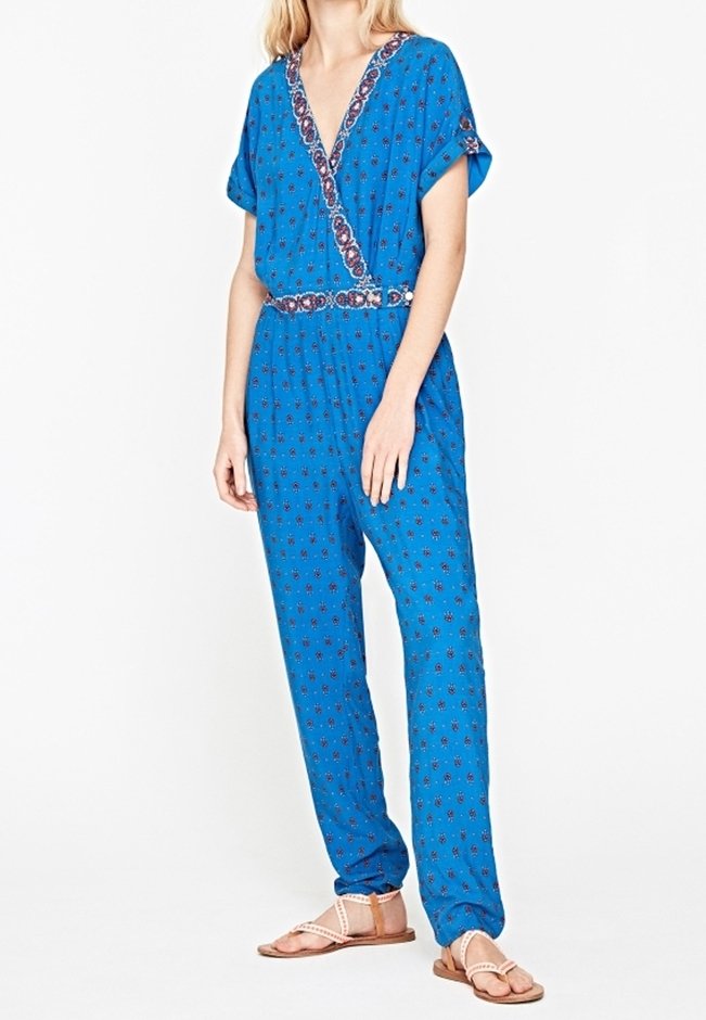 Combinaison bleue à manches courtes, col en V, avec des accents à motif floral. Caractérisée par une taille cintrée et des jambes larges et droites. Portée avec des sandales plates.