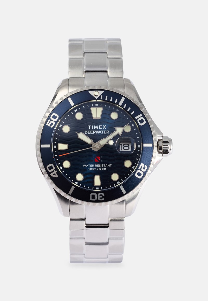 Timex Deepwater óra rozsdamentes acél karkötővel és kék, kerek számlappal, fehér órásjelzőkkel és 3 órakor elhelyezett dátumablakkal.