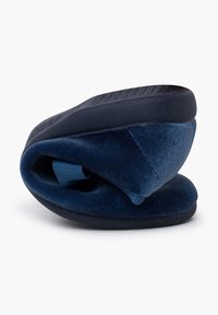 Zapato de lona azul marino sin cordones con un upper suave y aterciopelado y suela de goma. El zapato está enrollado, mostrando su forma redondeada y diseño flexible.