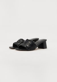 Black leather block-heeled sandals featuring a woven upper, open toe, and smooth texture. The heel height is moderate, providing stability.