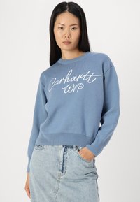 Blue sweater made of soft material, featuring a round neck and long sleeves. Notable white "Carhartt WIP" text on the front.