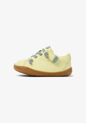 Gul lädersko med grå skosnören och en beige gummisula. Har rundad tå och ett kardborreband med en liten logotyp.