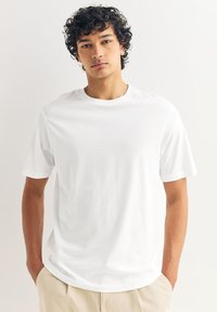 Bijela pamučna majica s kratkim rukavima i okruglim izrezom, s opuštenim krojem i glatkom teksturom. Bez vidljivih uzoraka ili naglasaka.