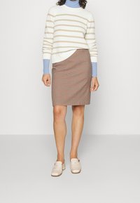 Suéter rayado en crema y beige con punto texturizado. Falda a cuadros marrón con un diseño de envoltura diagonal. Mules de color claro completan el atuendo.