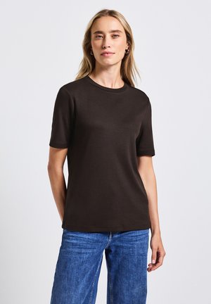 T-shirt in cotone marrone con maniche corte, scollatura rotonda e vestibilità rilassata, abbinato a jeans in denim blu chiaro. Design semplice, senza fantasie.
