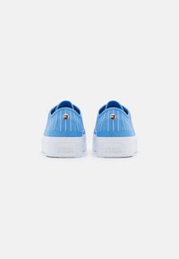 Sneakers in tela blu con suola piatta bianca texturizzata, caratterizzate da un'accenno del logo e strisce verticali bianche sul retro.
