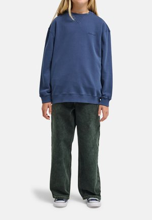 Granatowa bluza z dzianiny z prążkowanymi ściągaczami, zestawiona z zielonymi szerokimi spodniami. Na piersi znajduje się subtelne logo, a tkanina ma fakturę.