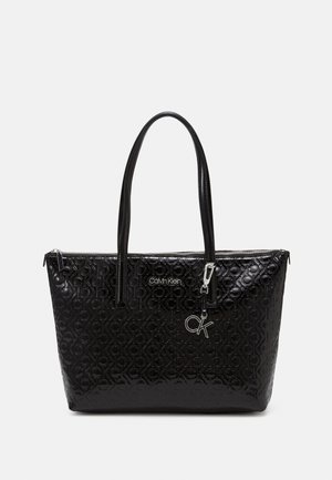 Black Calvin Klein tote bag with embossed CK logo pattern, silver zipper, double handles, and detachable silver CK charm on front.