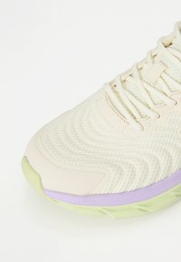 Ανοιχτόχρωμο παπούτσι τρεξίματος με υφασμάτινη επάνω επιφάνεια, με υφή, που διαθέτει παστέλ πράσινα και μωβ στοιχεία στη σόλ�α και ίσιους λευκούς κορδόνια.