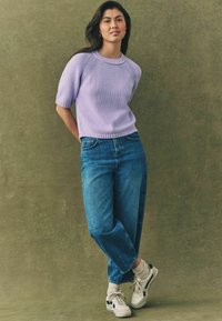 Maglione a maniche corte di colore lilla, lavorato a maglia, con colletto e polsini a coste, abbinato a jeans in denim blu a vita alta e sneakers bianche con dettagli neri.