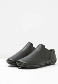 Zapatos negros de cuero sin cordones con un acabado suave, perfil bajo, acentos laterales elásticos y un diseño de puntera redondeada. Estilo cómodo y minimalista.
