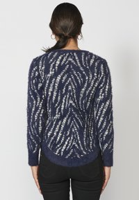 Suéter fuzzy de color azul marino con patrón de olas blancas, mangas largas y dobladillo redondeado. Textura suave y ajuste relajado.