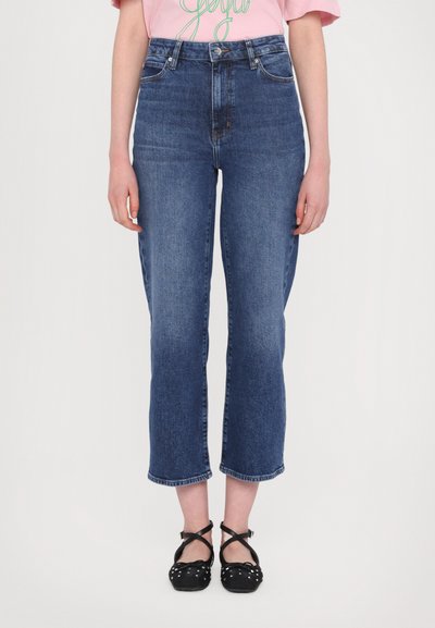 Jeans in denim blu ad alta vita con taglio gamba cropped, caratterizzati da una leggera scoloritura e un classico design a 5 tasche. Abbinati a scarpe nere con cinturini.
