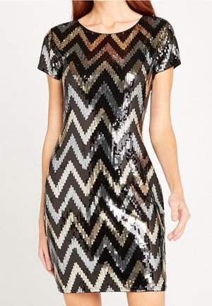 Femme portant une robe courte à manches courtes, longueur genou, avec un motif zigzag de sequins noirs, argentés et dorés.