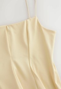 Vestido sin mangas de color crema con tirantes finos y detalles sutiles de costuras verticales en la tela.