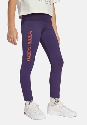 Paarse leggings met de tekst "Minnie Mouse" in oranje. Gemaakt van rekbare stof met een aansluitende pasvorm. Gecombineerd met witte sneakers en gestreepte sokken.