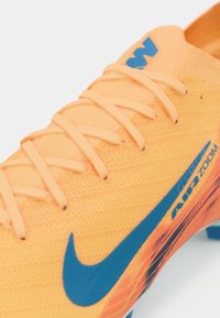 Narancssárga sportcipő, textúrált anyagú felsőrésszel, kék swoosh logóval és élénk fűzőkkel. Az oldalon "AIR ZOOM" márkajelzés található.