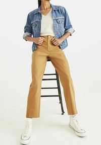 Ljusblå denimjacka med uppvikta ärmar, vit t-shirt med v-ringning och högmidjade, bruna byxor. Vita sneakers med snörning.