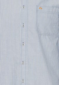 Striped button-up shirt in light blue and white. Features a chest pocket with a small orange logo. Made of lightweight fabric with a smooth texture.