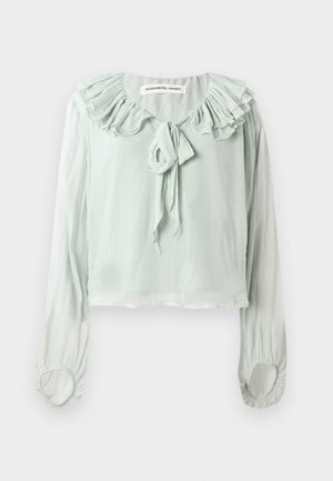 Blouse vert clair avec un col à volants, un détail à nouer et des manches longues. Fabriquée en tissu doux et fluide avec des poignets froncés.
