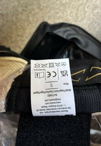 Schwarzer Stoffriemen mit strukturierter Oberfläche, mit Pflegeetikett, das Waschsymbole und die Größe 8 zeigt, teilweise sichtbar.