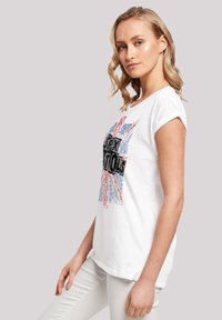 White cotton t-shirt with short sleeves featuring a Union Jack graphic, black text, red accents, and blue details. Smooth texture.