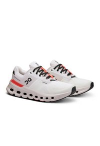 Witte hardloopschoenen met zwarte veters en accenten. Bovenwerk van mesh, dikke gevoerde zool met roze en zwarte details, met hexagonale uitsparingen.