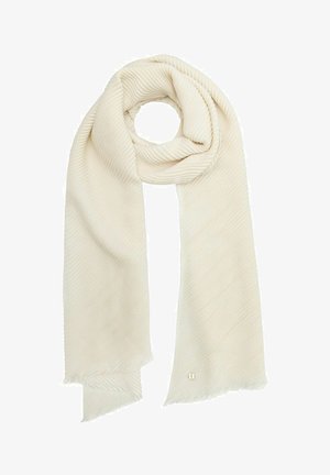 Jasno kremowy, prążkowany szalik o miękkiej teksturze, luźno ułożony z frędzlami na końcach oraz małym złotym emblematem blisko jednego końca.