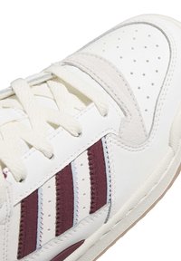Witte sneaker met textuurleer en nubuck accenten. Voorzien van drie bordeauxrode strepen, een geperforeerd ontwerp, platte veters en een rubberen zool.