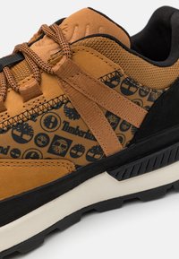 Baskets marron alliant suède lisse et textile à motif. Accents noirs et semelle épaisse texturée avec un motif de crampons visible.