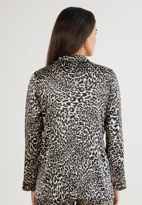 Béžový a černý top s leopardím vzorem a dlouhým rukávem, s volným střihem, límečkem a hladkou texturou. Viditelné švy a detaily šití.