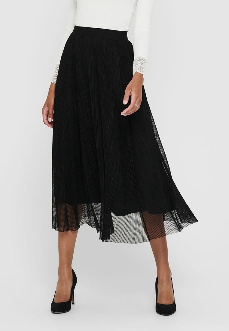 Jupe midi plissée noire avec une large ceinture, texture aérienne et une couche transparente, associée à des chaussures à talons hauts noires.