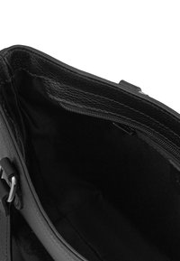 Intérieur d'un sac à main en cuir noir avec une poche zippée. Surface texturée et doublure lisse avec un grand compartiment ouvert.