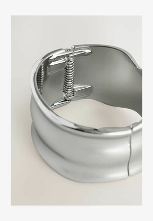 Hõbedane metallist käevõru, millel on sile pind, varustatud vedrumehhanismiga ja läikiva, peegeldava viimistlusega. Sümboliteta.