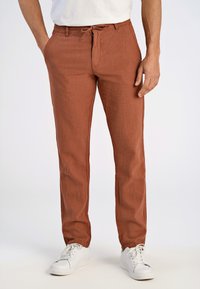 Roodbruine linnen broek met een elastische tailleband, een trekkoord en zijzakken, gecombineerd met witte sneakers.