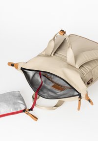 Zaino beige con esterno trapuntato, dettagli in pelle e interno a motivo grigio a rete. Include una borsa grigia rimovibile con zip rossa.