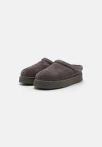 Dark gray slip-on clogs made of soft suede with a rounded toe and a textured rubber sole. Feature a cushioned rim and minimal stitching detail.
