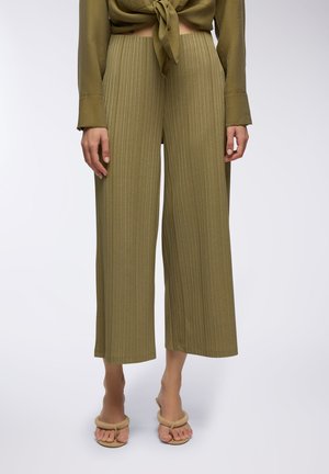 Pantaloni a gamba larga in tessuto verde oliva con coste; presentano una vita alta e una finitura texture. Abbinati a sandali leggeri con punta aperta.
