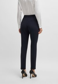 Marineblauwe broek met een verzamelde elastische tailleband, zijzakken en een slim fit, gedragen met zwarte hoge hakken en een witte button-up blouse.