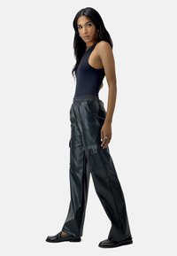 Svart ärmlös bodysuit som är parat med hög midja svarta fusk-läder cargobyxor med sidofickor och en avslappnad passform. Svarta loafers.