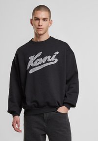 Sort sweatshirt med et stort, hvidt "Kani" logo på brystet, rund halsudskæring og afslappet pasform med ribbede manchetter og kant.