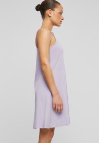 Robe sans manches en lavande clair, fabriquée dans un tissu doux. Sa forme évasée présente une texture lisse et des détails de couture minimalistes.