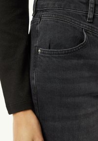 Schwarze Jeans aus Denim mit einer enganliegenden Passform, die über eine Seitentasche und sichtbare Nähte verfügt. Die Textur wirkt glatt und leicht ausgebleicht.