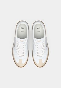 Adidași albi cu accente din suede bej, având vârful rotund, șireturi și brandul "BOSS" pe laturi și pe tălpic. Talpă din cauciuc.