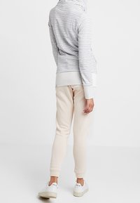 Sudadera con capucha a rayas grises y blancas combinada con pantalones de chándal beige y zapatillas blancas, vista desde atrás. Presenta un corte relajado y una textura suave.